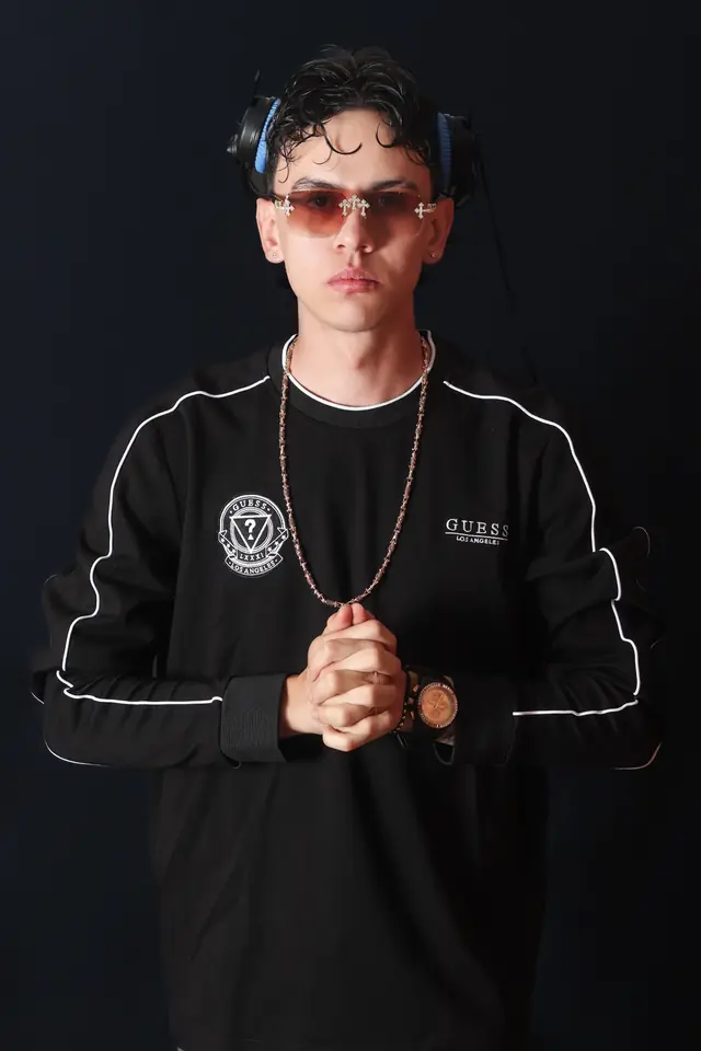 Artista con gafas y audífonos al cuello, manos juntas, sobre fondo negro