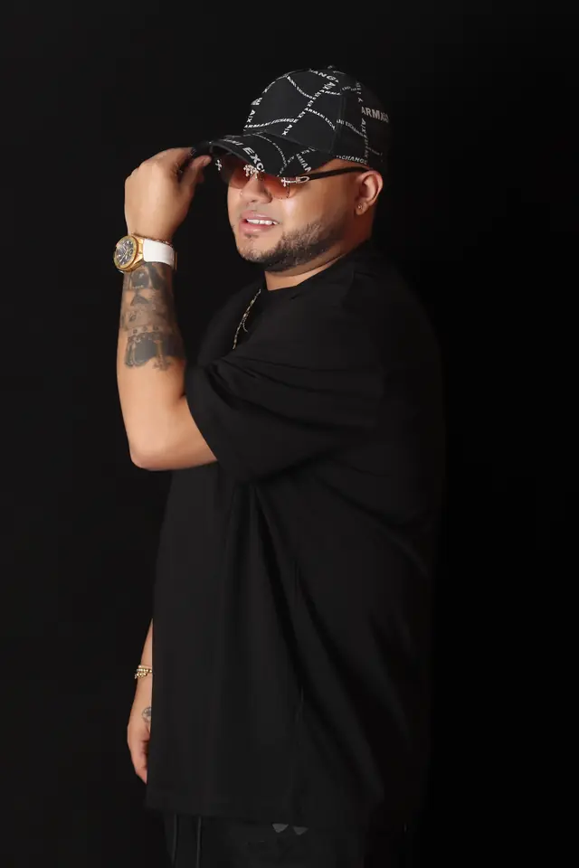 Artista de perfil con gorra y ropa negra sobre fondo negro