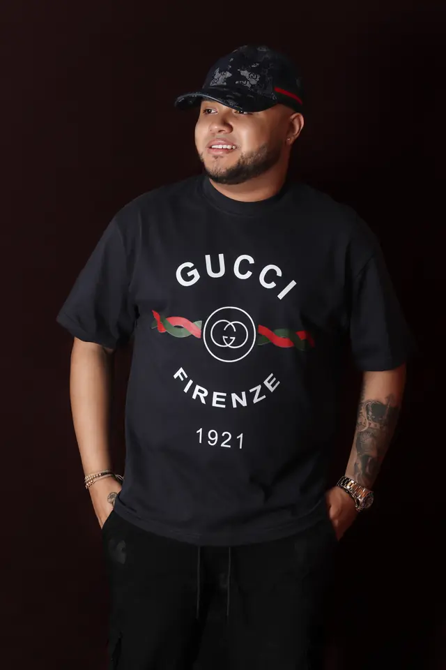 Retrato de estudio de un artista con gorra y camiseta negra, manos en los bolsillos