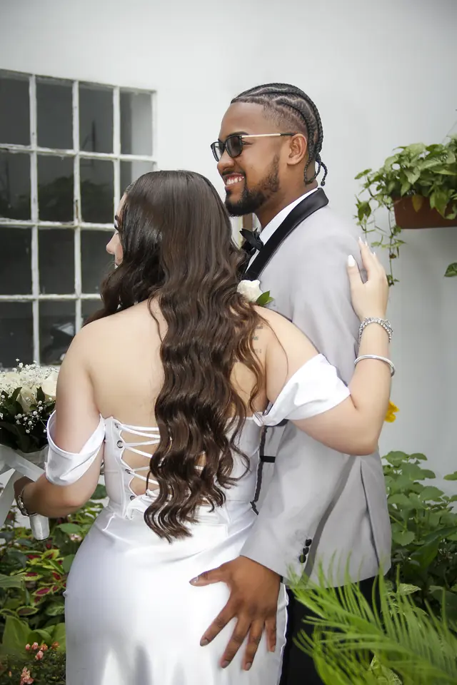 Novios abrazados en un jardín, ella de espaldas con vestido blanco