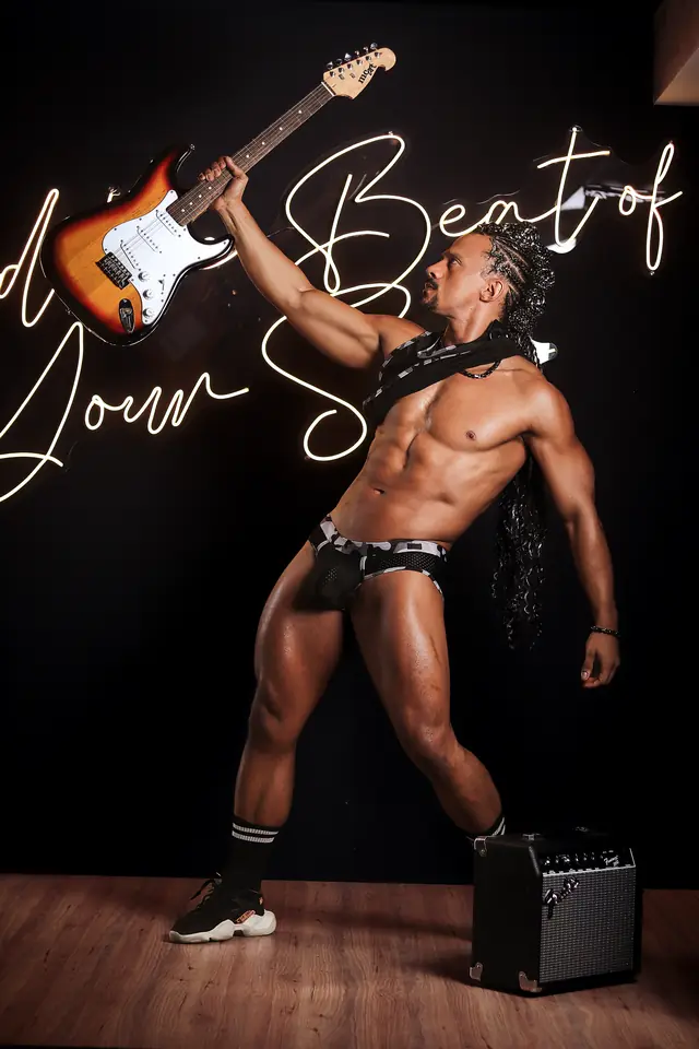 Hombre que levanta una guitarra eléctrica frente a un letrero de neón