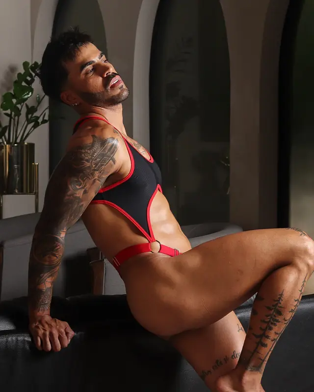 Hombre tatuado con body negro y rojo recostado en un sofá