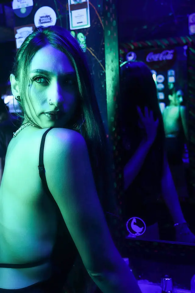 Mujer de espaldas que mira a la cámara bajo luz verde y azul en un bar