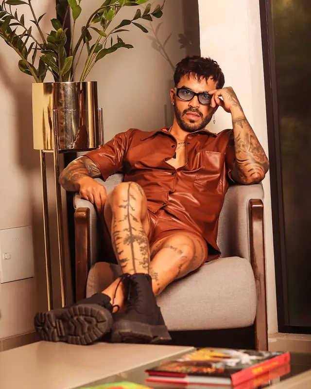 Hombre con conjunto de cuero café y gafas, sentado en un sillón