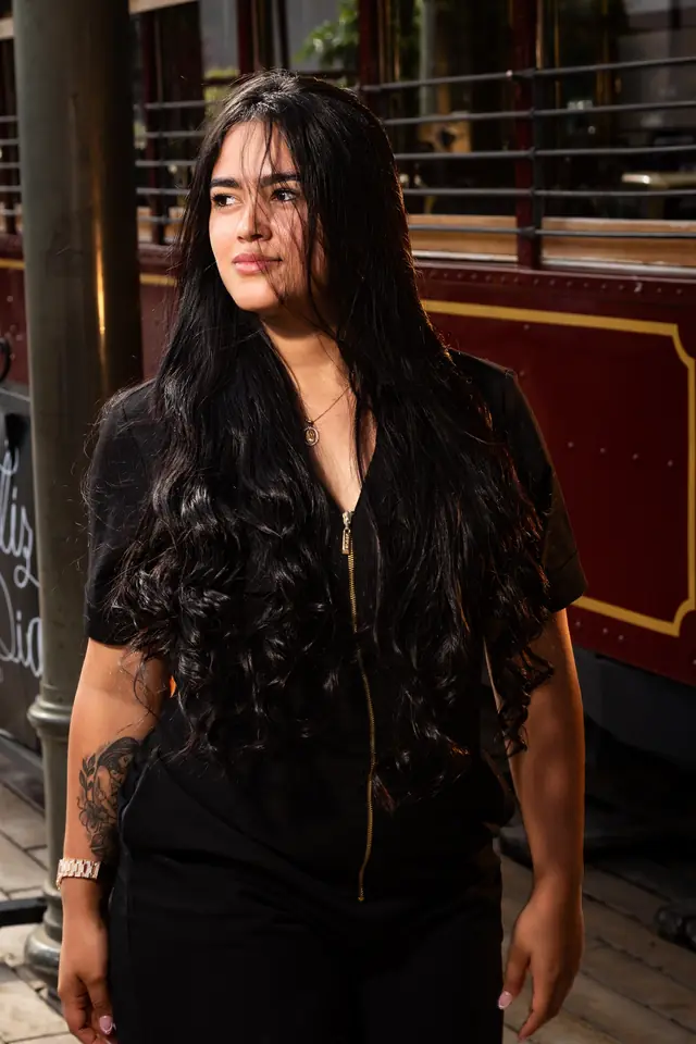 Retrato de una mujer de cabello largo y ropa negra junto a un vagón antiguo