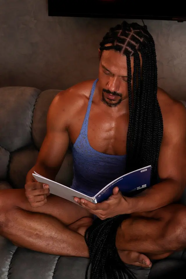 Hombre de trenzas largas que lee una revista sentado en un sofá