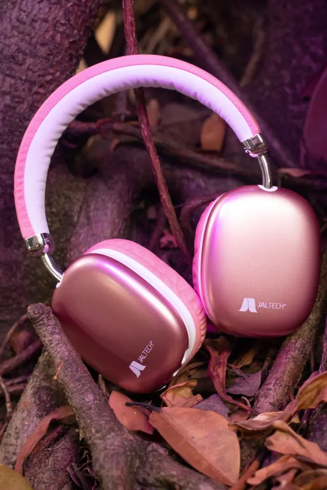 Audífonos rosados de diadema sobre raíces y hojas secas
