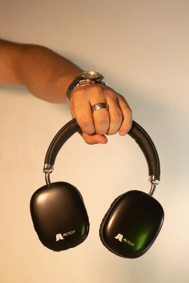 Mano que sostiene unos audífonos negros de diadema sobre fondo claro