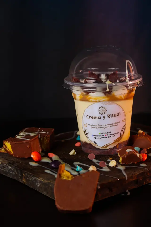 Postre en vaso con tapa domo sobre tabla de pizarra, rodeado de trozos de chocolate