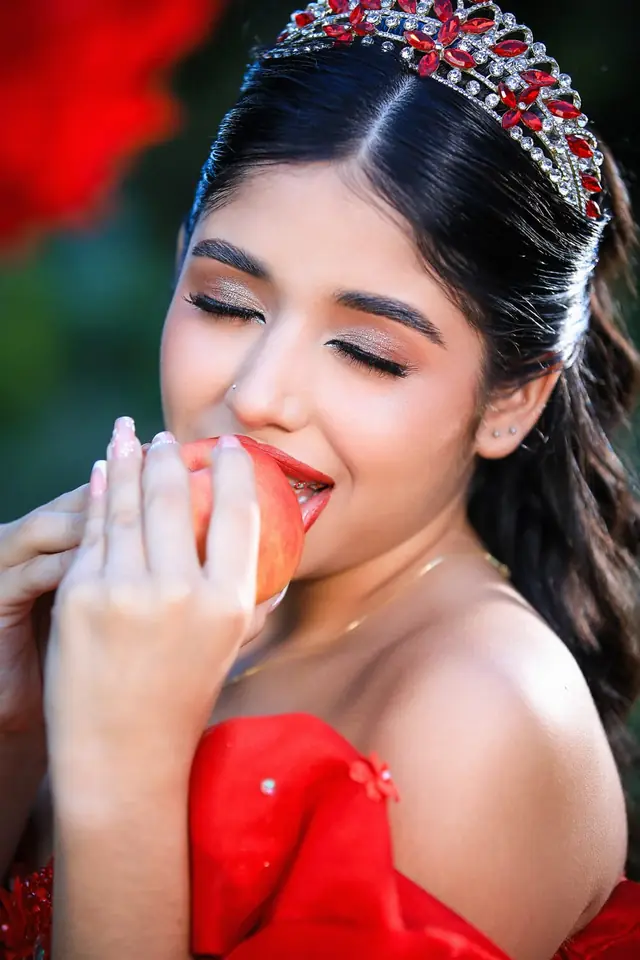 Primer plano de una quinceañera con tiara que muerde una manzana