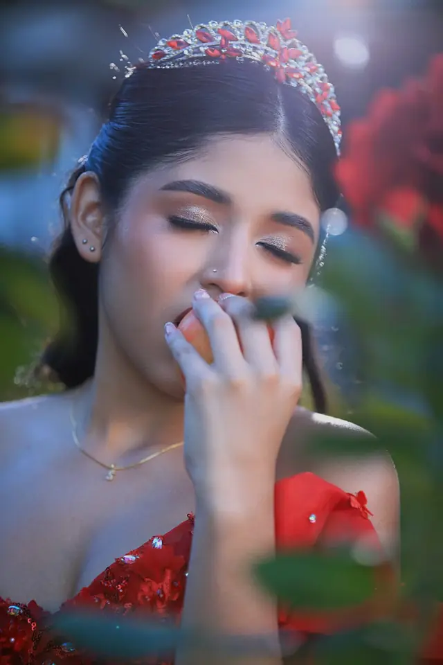 Retrato de una quinceañera con tiara entre flores rojas