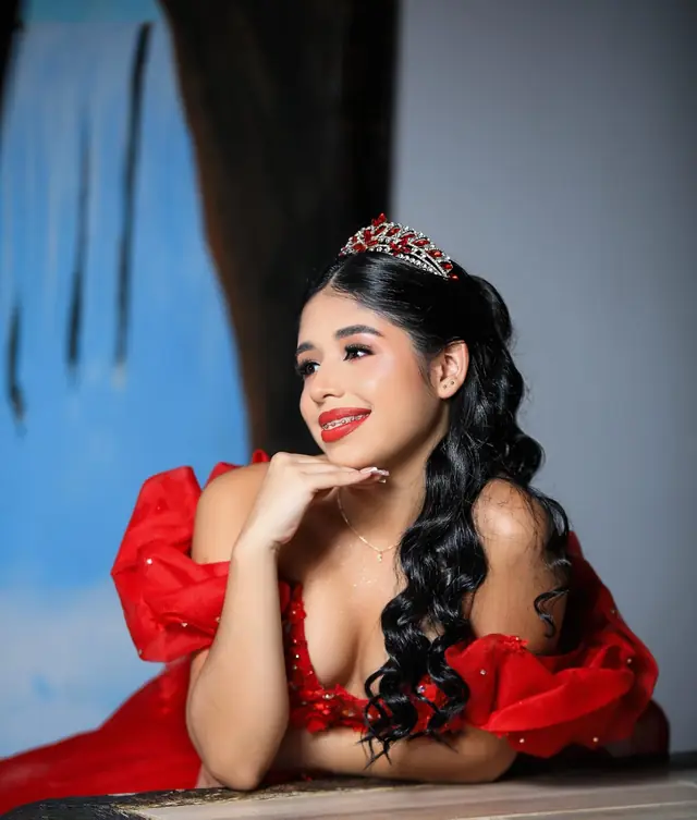 Quinceañera con tiara apoyada sobre una mesa, sonriendo