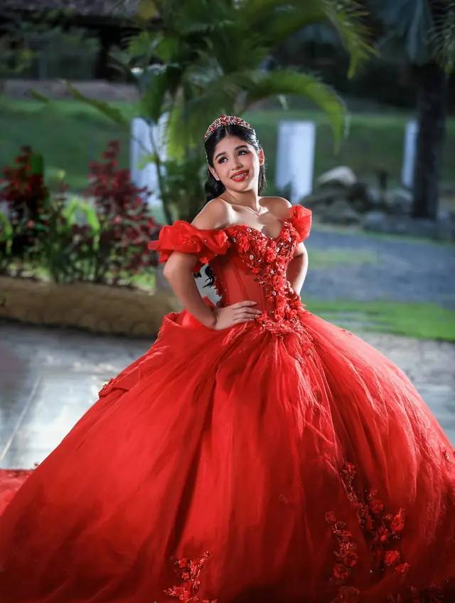 Quinceañera con vestido rojo de vuelo y tiara en un jardín