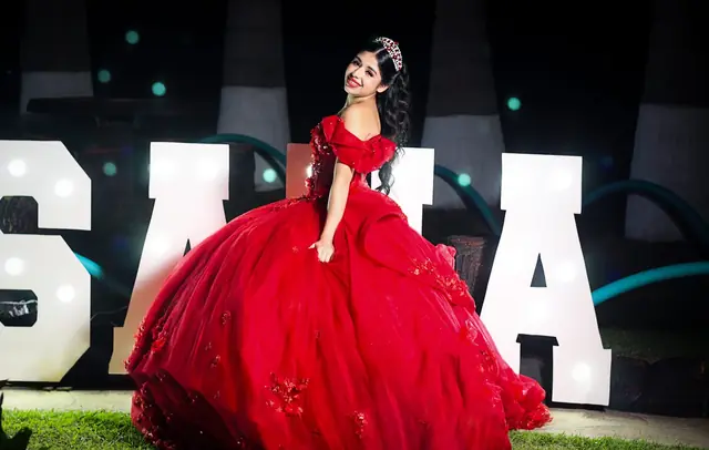 Quinceañera con vestido rojo sentada frente a letras luminosas, de noche